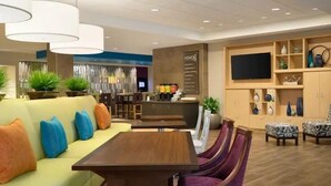Un moderno vestíbulo de hotel con un sofá amarillo, sillas moradas, una mesa de madera y un mostrador de recepción.
