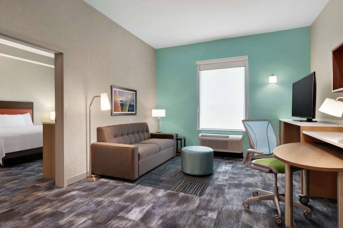 A hotel room with a bed, a sofa, a desk, a chair, a TV, and a window.
