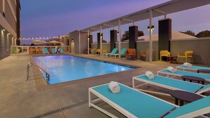 Un área de piscina en la azotea con sillones y sombrillas.