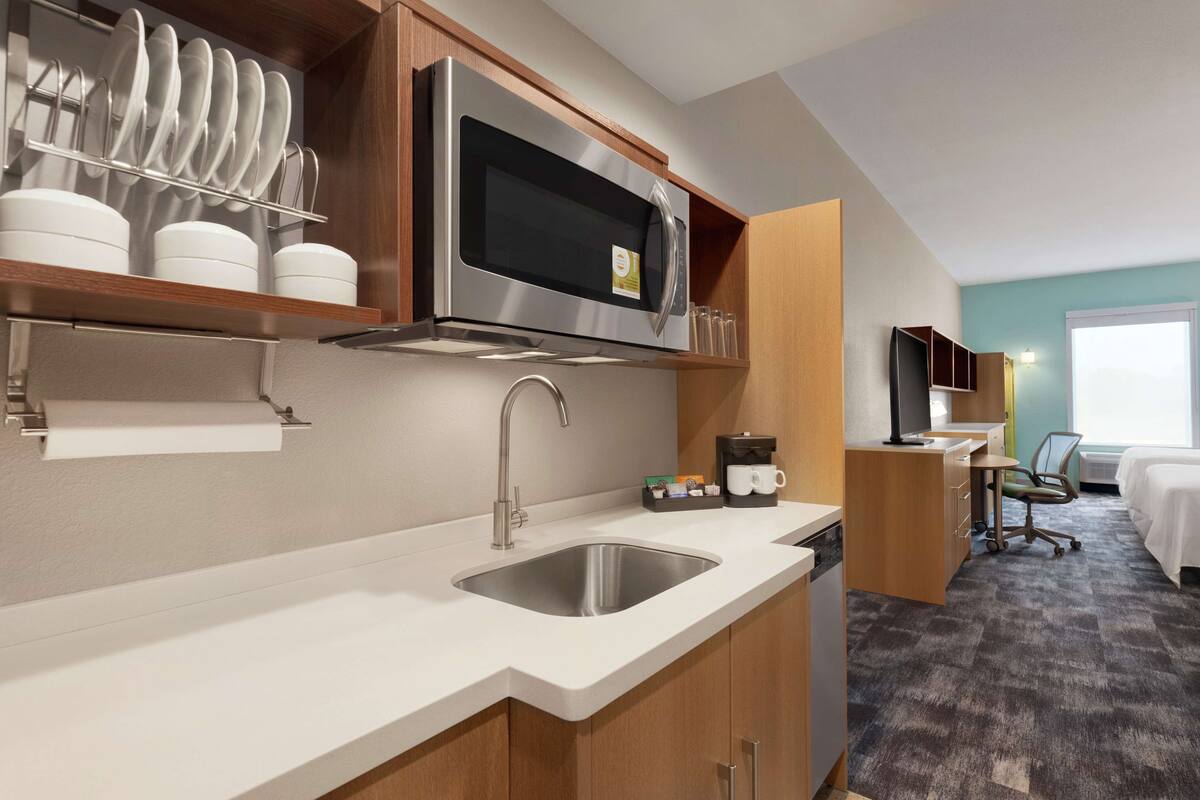 A modern kitchen with a stainless steel sink, a microwave, and dish drying racks.