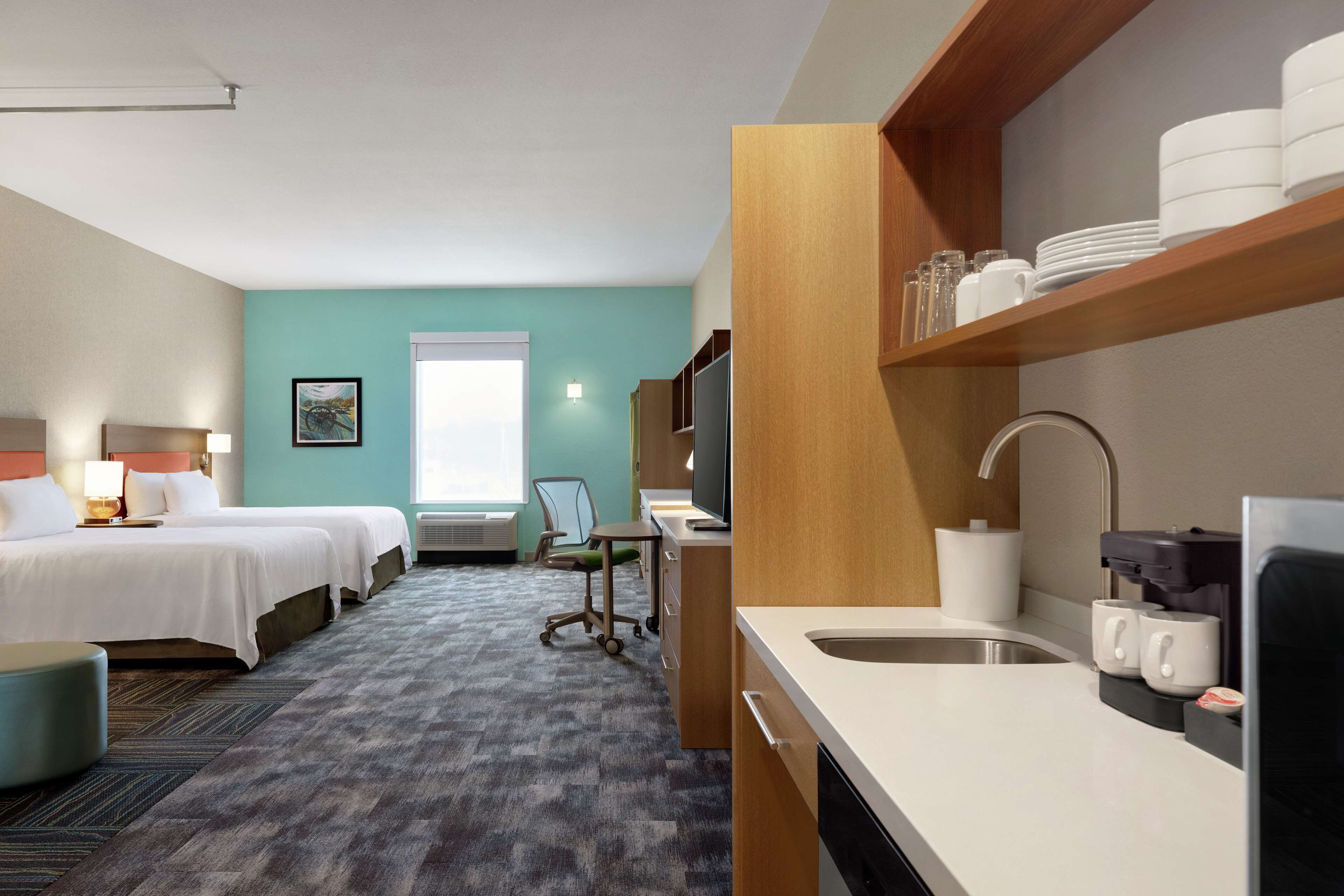Een hotelkamer met twee bedden, een bureau, een kitchenette en een raam met uitzicht.