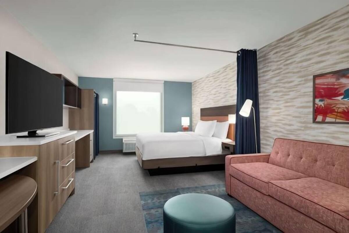 A hotel room with a bed, a desk, a television, a sofa, and a painting on the wall.