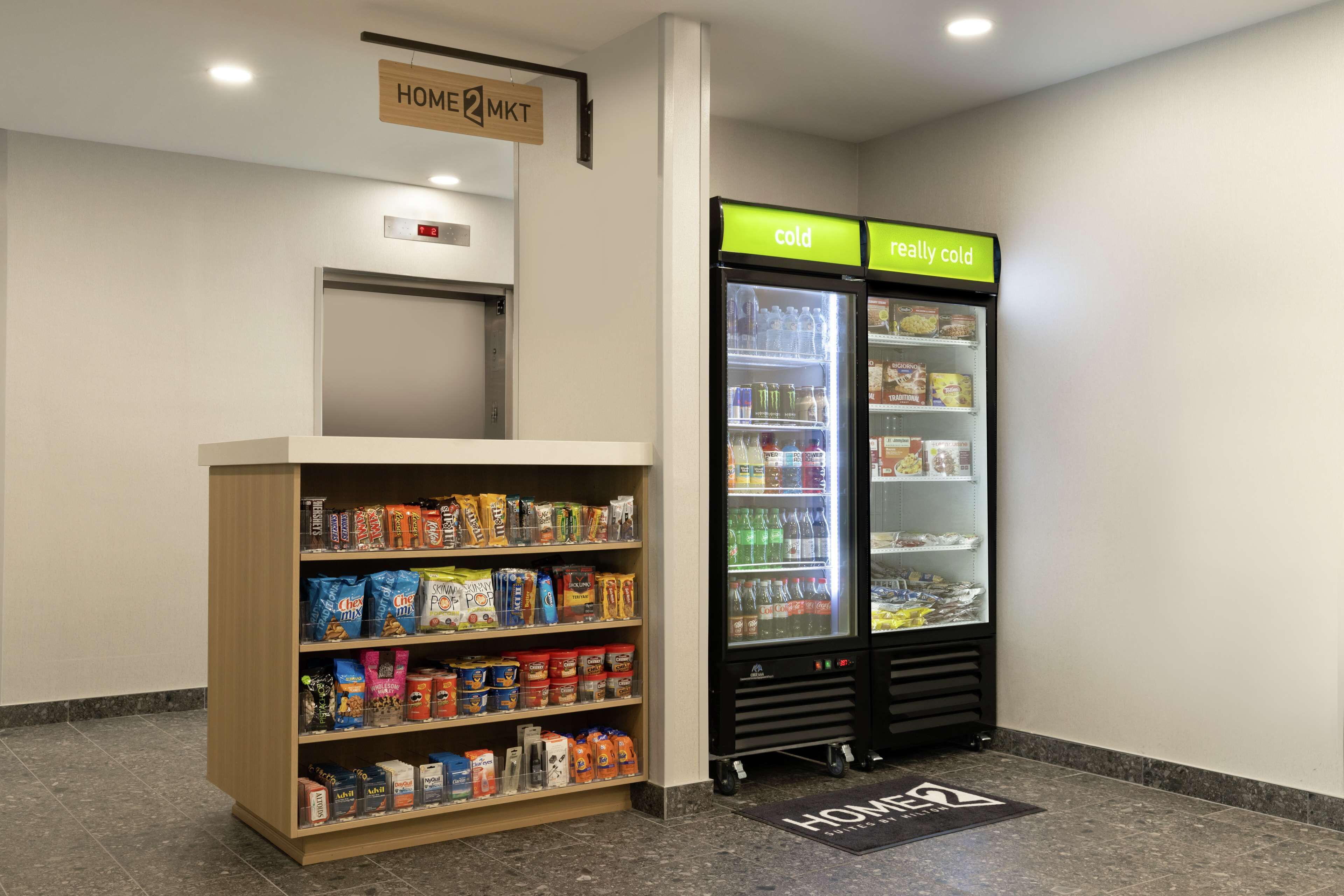 A self-service kiosk with a variety of snacks and beverages, a refrigerator labeled 'cold' and 'really cold', and a 'HOME2MKT' sign above the door.