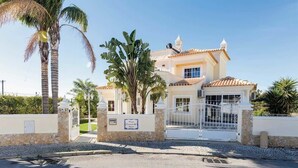 Una casa de dos pisos con techo de tejas, entrada con portón y muro de piedra.