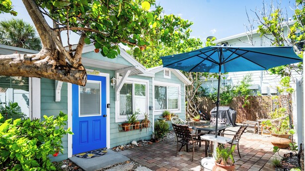 Un patio con una mesa y sillas, una sombrilla azul y plantas en macetas.
