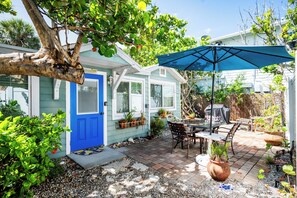 Un patio con una mesa y sillas, una sombrilla azul y plantas en macetas.