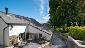 A white building with a stone foundation, a tiled roof, and a paved patio with outdoor furniture. - A luxury rural retreat, Barnstaple, perfect for couples and families, set in glorious North Devon (Barnstaple)