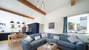 A modern living room with a sectional sofa, wooden dining table, and a kitchen in the background. - A luxury rural retreat, Barnstaple, perfect for couples and families, set in glorious North Devon (Barnstaple)