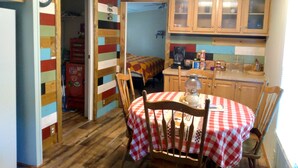 Une cuisine de taille modeste, avec des meubles de rangement en bois, une table à manger recouverte d’une nappe à carreaux et une horloge au mur.