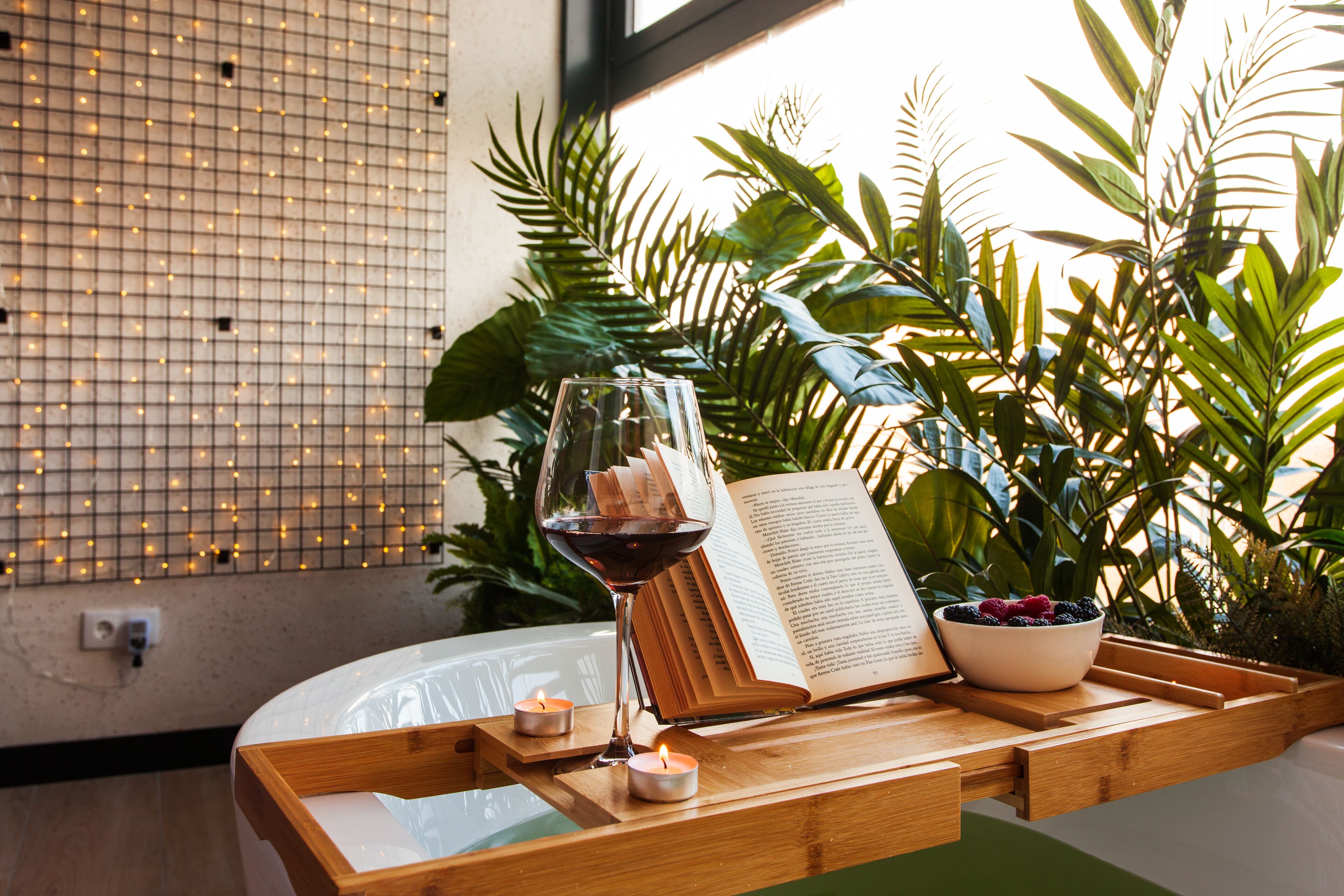 Una bandeja de madera con una copa de vino tinto, un libro abierto y un bol de bayas.