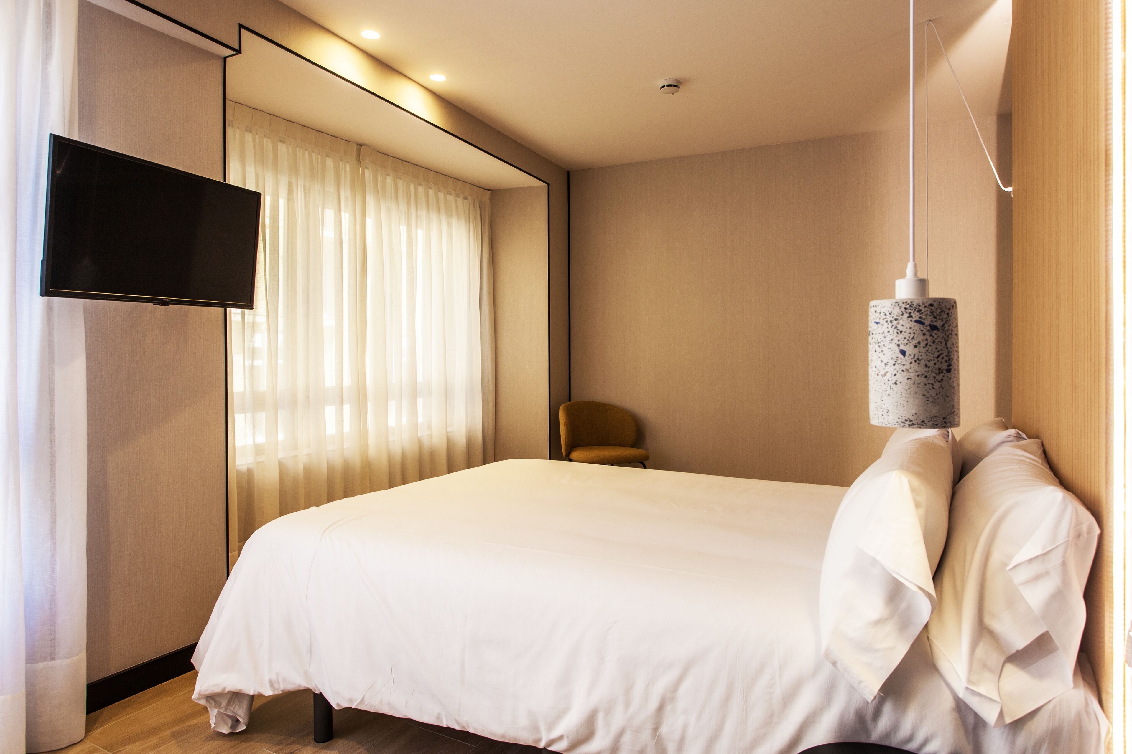 Una habitación de hotel moderna con una cama grande, un televisor de pantalla plana montado en la pared y una lámpara colgante.