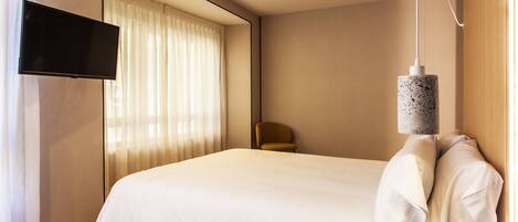Una habitación de hotel moderna con una cama grande, un televisor de pantalla plana montado en la pared y una lámpara colgante.
