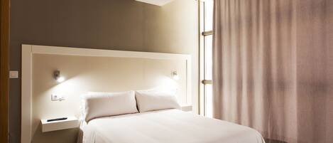 Un dormitorio con una cama grande, una mesita de noche y una ventana con cortinas.