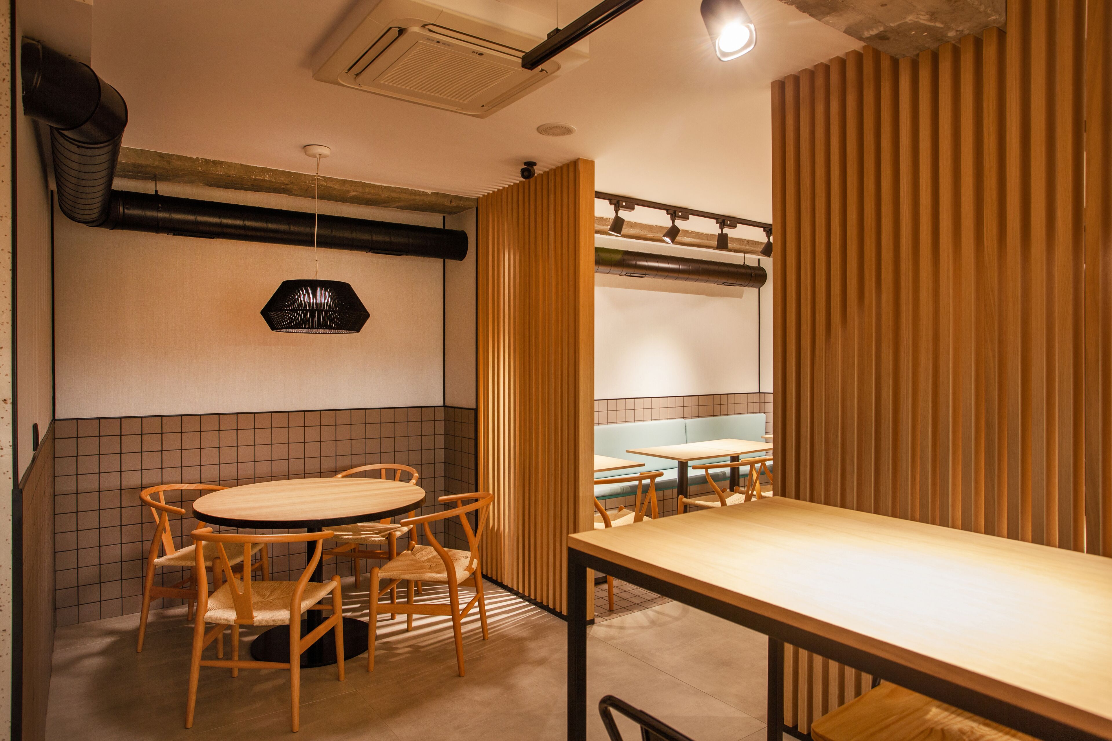 Interior de un restaurante con una mesa redonda y sillas, un separador de madera y una zona con bancos.