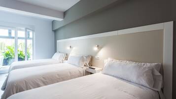 A hotel room with two beds, a large window, and a view of greenery outside.