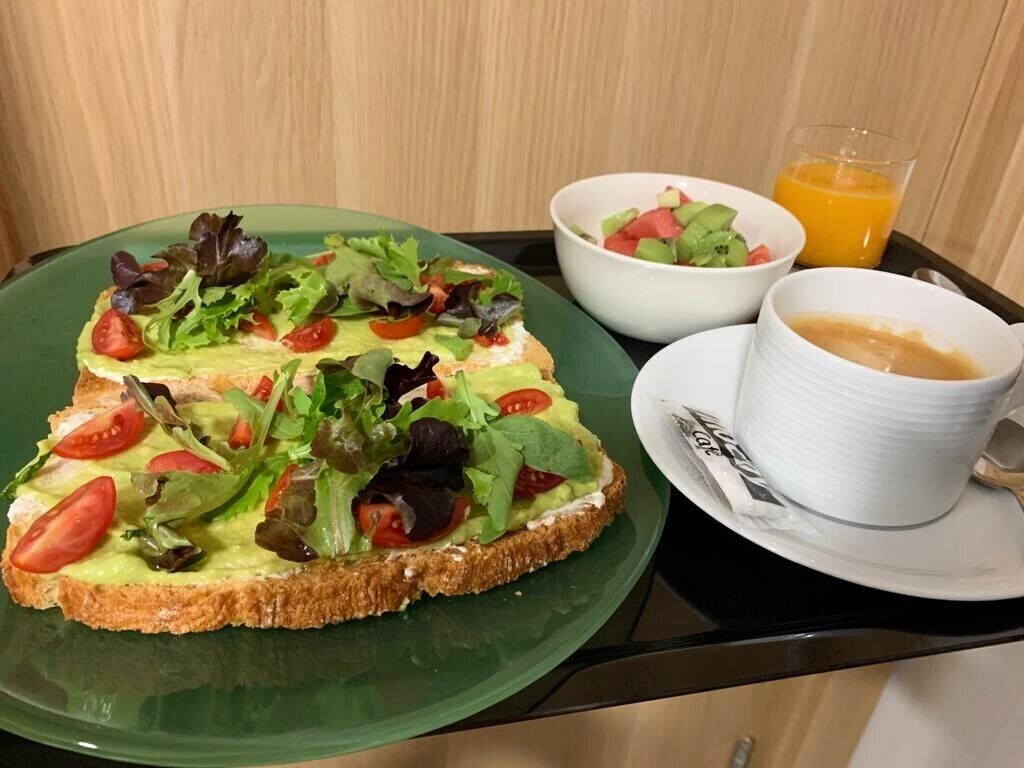 A breakfast tray with toast topped with avocado and greens, a bowl of salad, a glass of orange juice, and a cup of coffee.