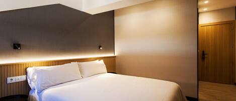 Una habitación de hotel moderna con una cama grande, un cabecero de madera, una mesita de noche y una puerta de madera.