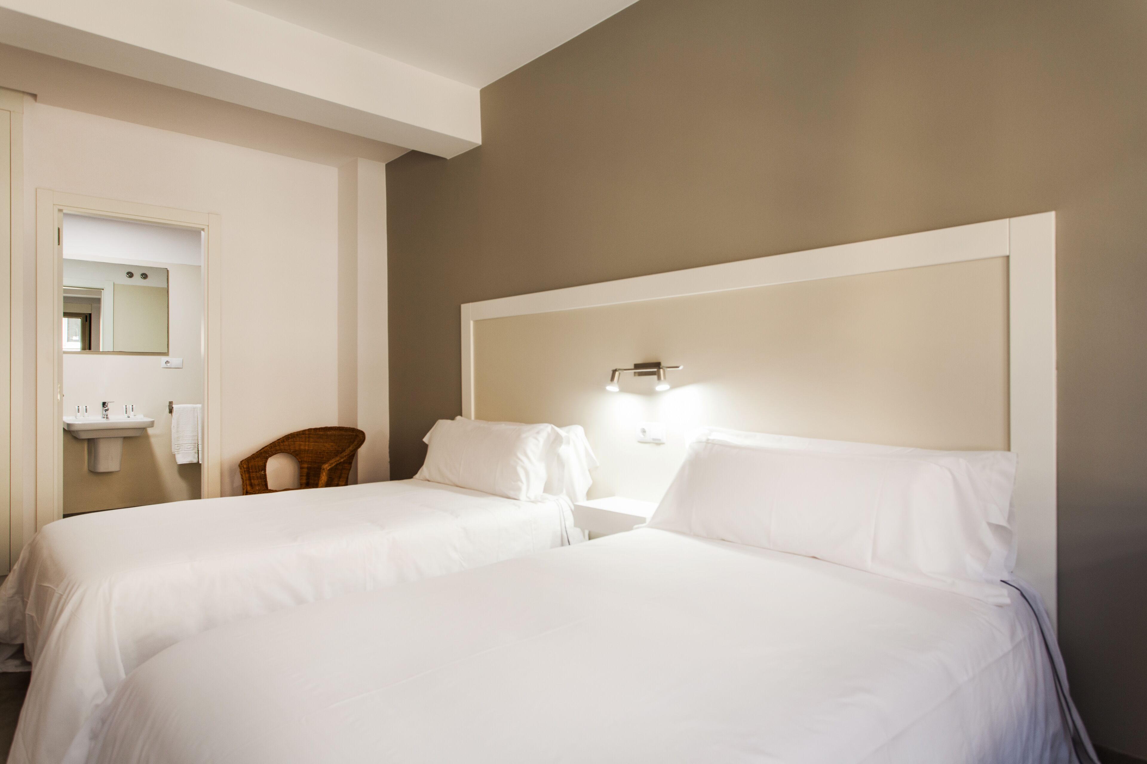 A hotel room with two beds, a small bathroom with a sink, and a mirror.