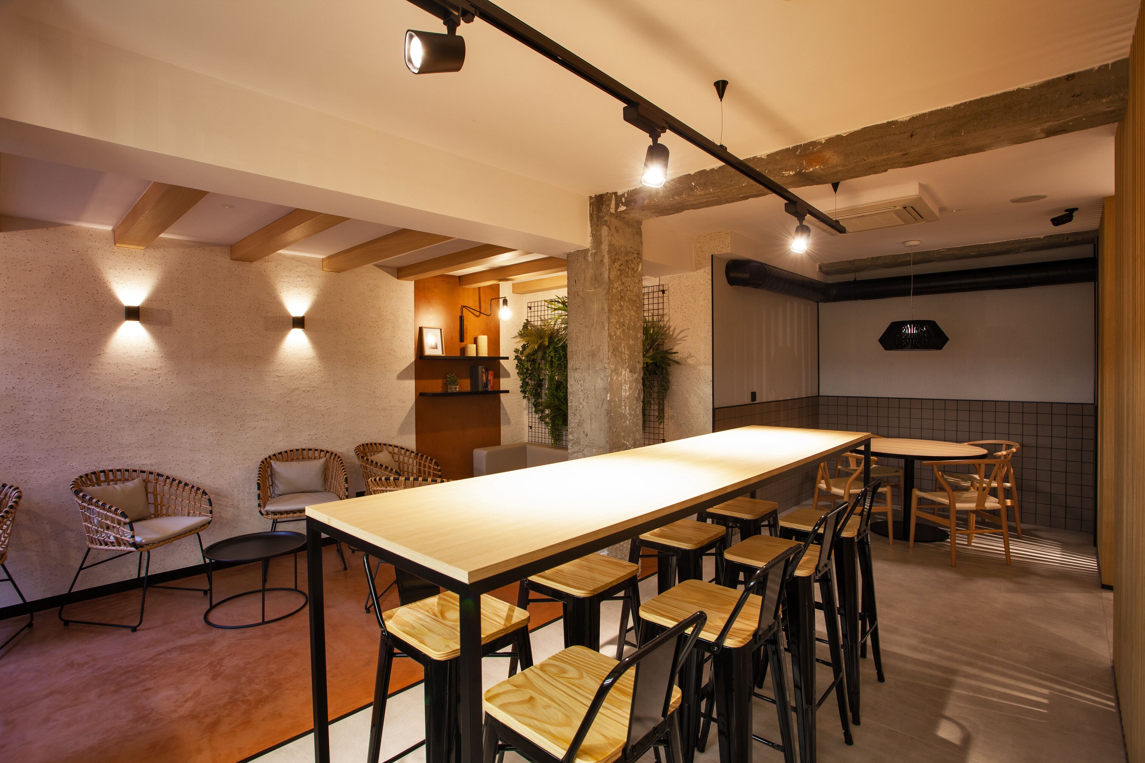 Un comedor moderno con una mesa larga y múltiples sillas, vigas de madera en el techo y una combinación de iluminación natural y artificial.