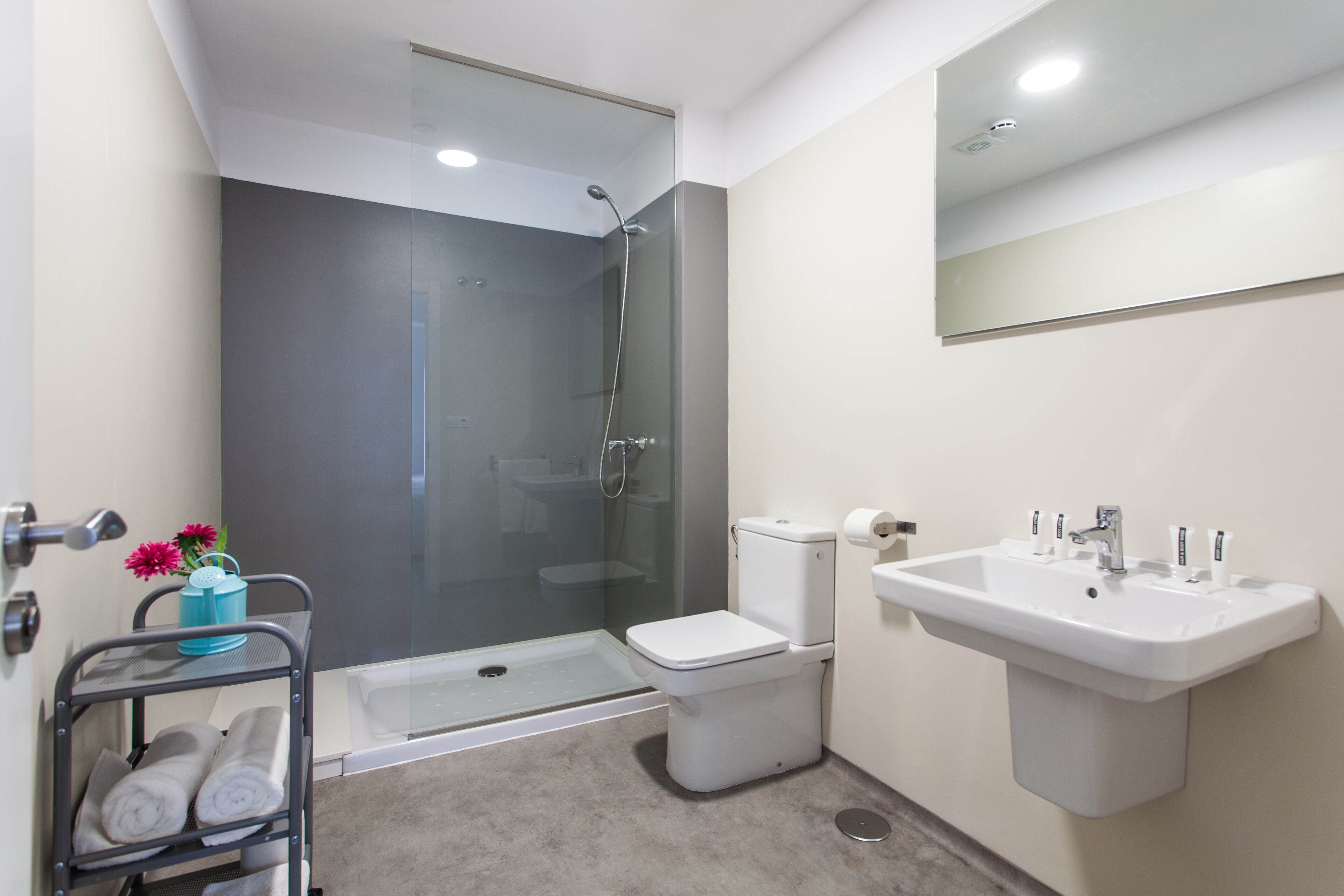 Un baño moderno con cabina de ducha de vidrio, inodoro blanco y lavamanos con espejo.