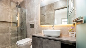 A modern bathroom with a glass-enclosed shower, a white toilet, and a large mirror above a sink with a plant. - Room 7 @ Pelican Paros in the Old Town (Paros)