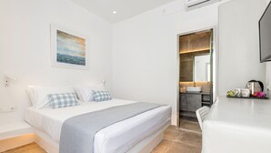 A modern hotel room with a bed, a bathroom with a sink and mirror, and a flat-screen TV on a table. - Room 7 @ Pelican Paros in the Old Town (Paros)