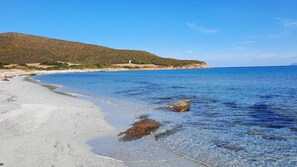 A beach with clear shallow waters, a sandy shore, and a hill in the background. - T2 neuf-VUE MER-CLIMATISE-WIFI-PISCINE- 4 personnes-Classé 3*** (Linguizzetta)