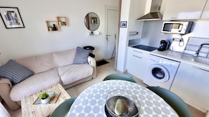 Um espaço compacto com cozinha compacta, máquina de lavar roupa, mesa de jantar e sofá.