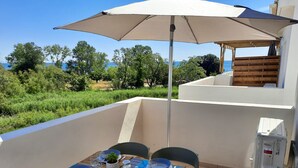 A dining area with a table set for four, an umbrella, and a view of the sea. - T2 neuf-VUE MER-CLIMATISE-WIFI-PISCINE- 4 personnes-Classé 3*** (Linguizzetta)