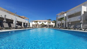 A clear blue pool with lounge chairs and umbrellas, surrounded by modern buildings with a clear sky above. - T2 neuf-VUE MER-CLIMATISE-WIFI-PISCINE- 4 personnes-Classé 3*** (Linguizzetta)