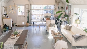 Ein geräumiges Loft mit hohen Decken, einem Essbereich, einem Wohnzimmer mit Sofa und Couchtisch sowie einem großen Fenster für natürliches Licht.