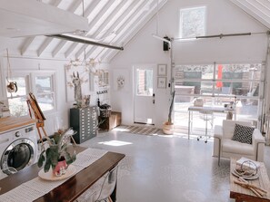 A spacious living room with a high ceiling, a dining area with a wooden table, and a view of the outside through large windows.