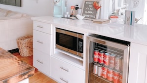 Eine moderne Küche mit weißen Schränken, einer eingebauten Mikrowelle, einer Kaffeemaschine und einem Kühlschrank mit Getränkespender.