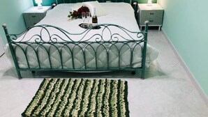 A bed with a metal frame and a white mattress, flanked by two bedside tables with lamps, in a room with teal walls and a patterned rug on the floor. - La Casetta di Angela - Bilocale (Marsala)