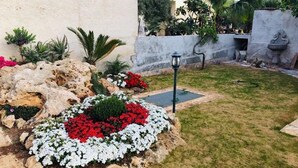 A landscaped garden with a rock formation, white and red flowers, and a lamp post. - La Casetta di Angela - Bilocale (Marsala)