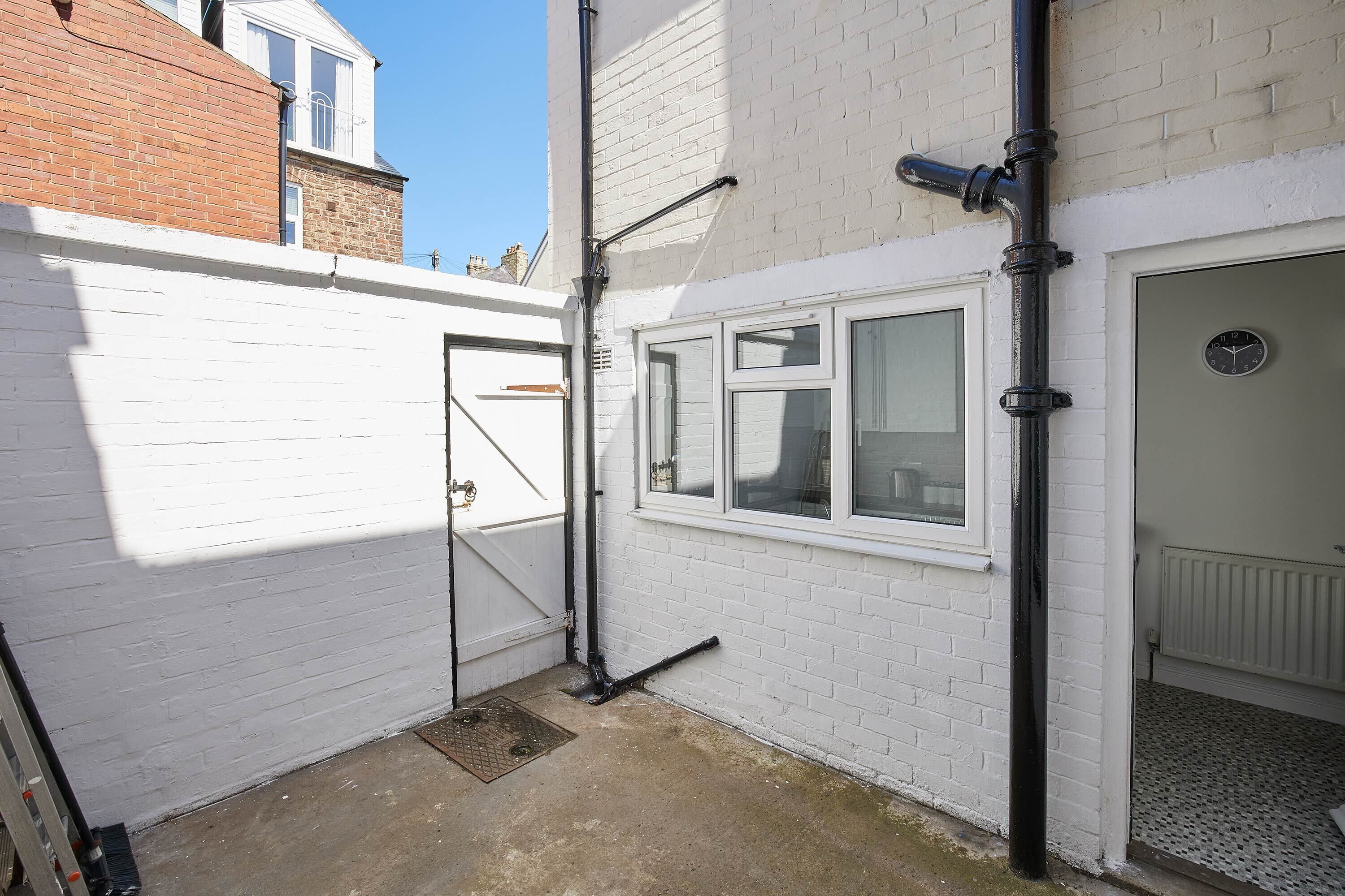 A narrow alleyway with a white brick wall, a metal gate, and a garage door.