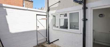 A narrow alleyway with a white brick wall, a metal gate, and a garage door.