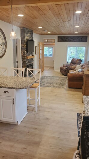 Relax in a warm and inviting living area with a high ceiling, stone wall, and large window offering a view of the outdoors.