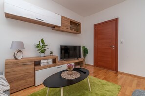 A modern living room with a TV, wooden furniture, a green rug, and a door. - Modern apt w. Terrace, 2 min Walk to the Beach (Okrug)