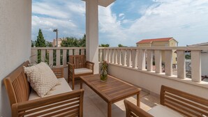 A balcony with wooden furniture, including a sofa and a table, and a view of buildings in the background. - Modern apt w. Terrace, 2 min Walk to the Beach (Okrug)