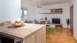 A modern living room with a wooden dining table, a TV, and a green rug. - Modern apt w. Terrace, 2 min Walk to the Beach (Okrug)