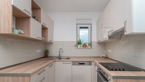 A modern kitchen with light wood cabinets, a built-in dishwasher, a stove, and a window above the sink. - Modern apt w. Terrace, 2 min Walk to the Beach (Okrug)