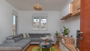 A modern living room with a grey sectional sofa, a small round table with a vase, a green rug, and a wooden cabinet with a plant. - Modern apt w. Terrace, 2 min Walk to the Beach (Okrug)