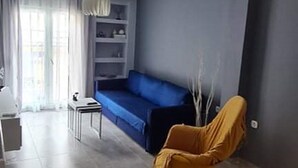 A modern living room with a blue sofa, a yellow armchair, and a dining area with a table and chairs. - Flat 66 (Thessaloniki)