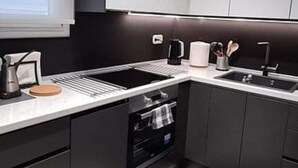 A modern kitchen with dark cabinetry, a white countertop, and a stainless steel sink. - Flat 66 (Thessaloniki)