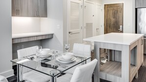 A modern kitchen with white cabinetry, a glass dining table, and white chairs. - Global Luxury Suites at Bethesda Metro (Bethesda)