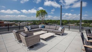 An outdoor seating area with a sofa, chairs, and tables, overlooking a cityscape. - Global Luxury Suites at Bethesda Metro (Bethesda)