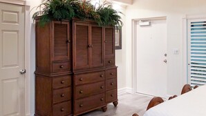 Une chambre à coucher avec une commode en bois, un lit recouvert d’une courtepointe blanche et une porte avec une fenêtre.