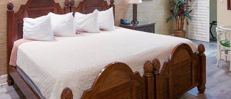 Una cama de madera con colchón acolchado, una mesita de noche con una lámpara y una planta en maceta.