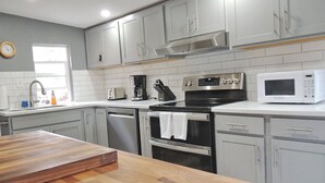 Une cuisine moderne avec des meubles gris, une cuisinière en acier inoxydable, un four à micro-ondes et une table en bois.